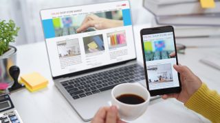 A person using a phone and laptop with a cup of coffee